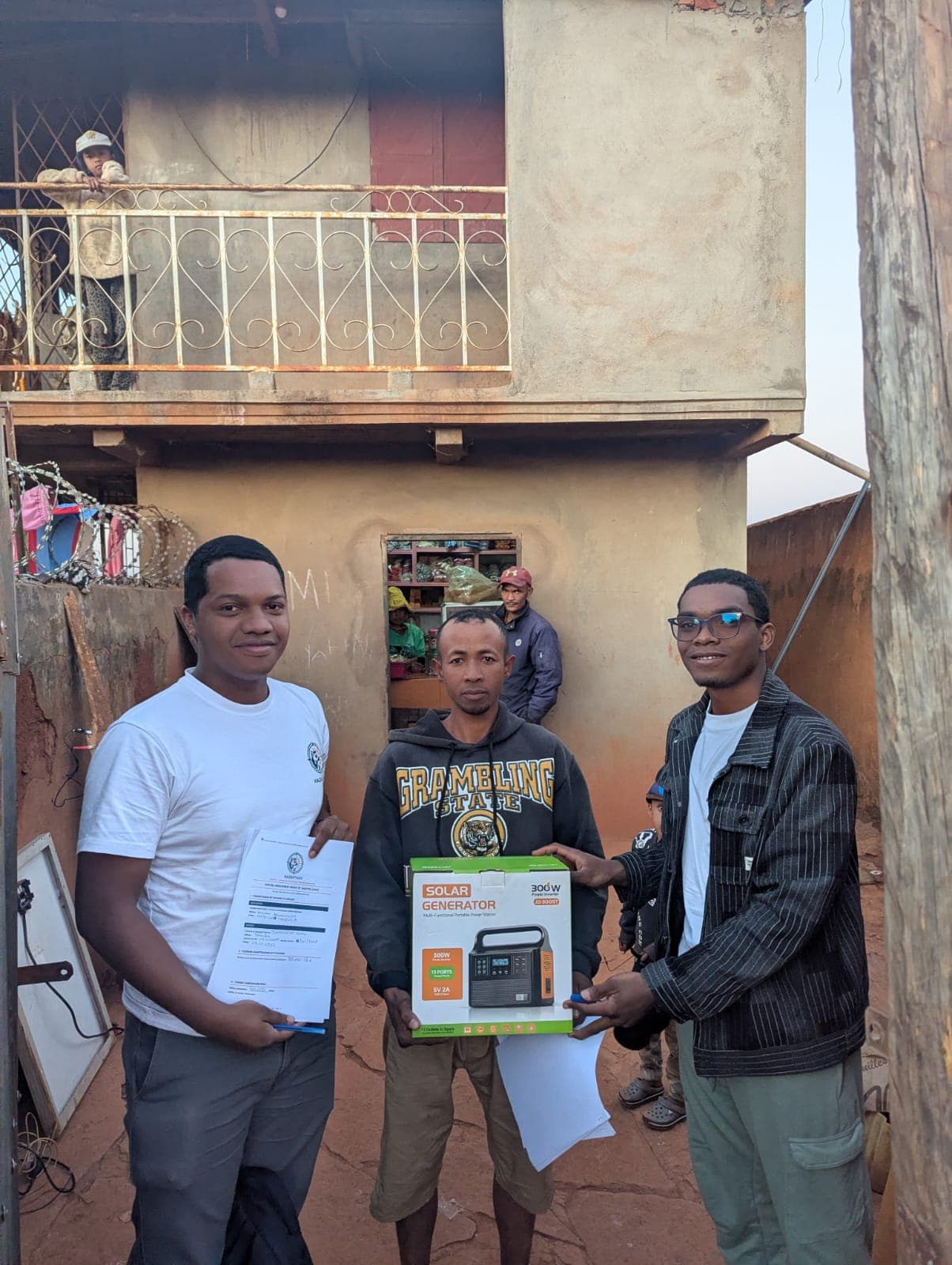 Remise d'un générateur solaire 300 W et du contrat signé à un client, devant sa maison dans un quartier d'Antananarivo